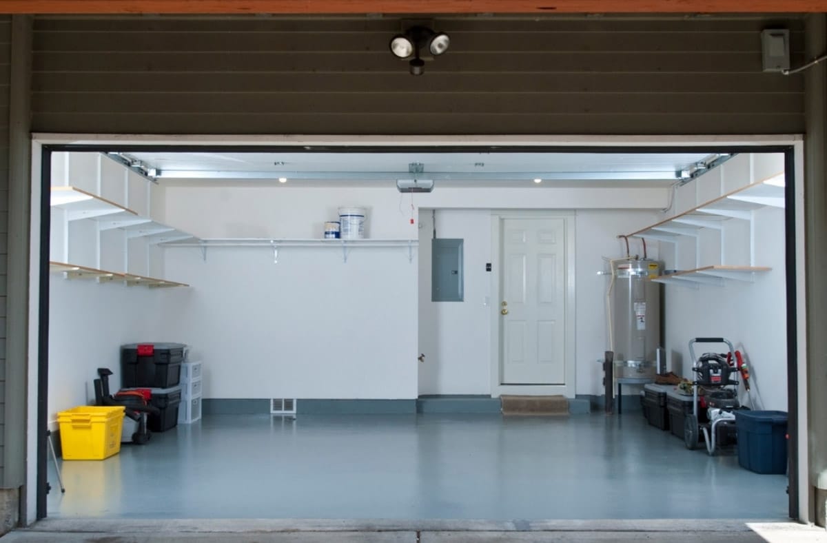 View from outside into a tidy, well-organized garage with open shelves, storage containers, a water heater, and a closed white door.